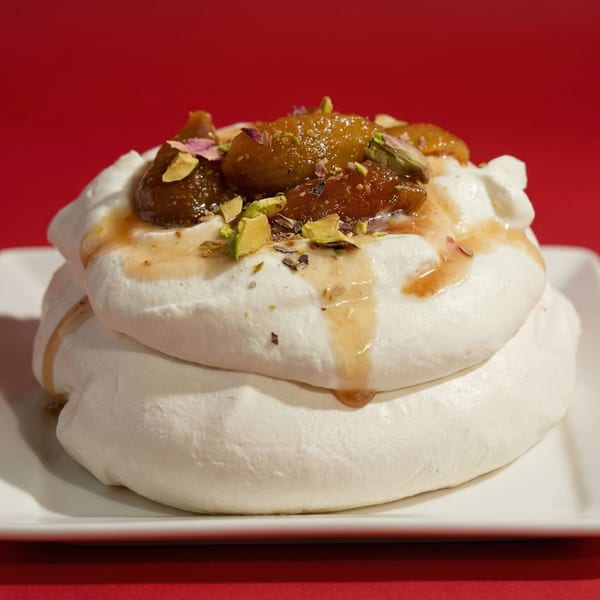 White meringue dessert topped with caramelized figs, pistachios, and a drizzle of syrup on a red background.
